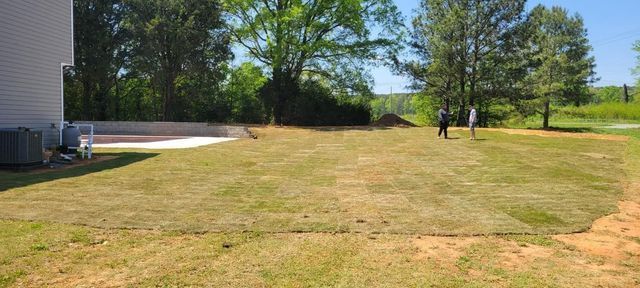 A large lawn with a house in the background and trees in the background.