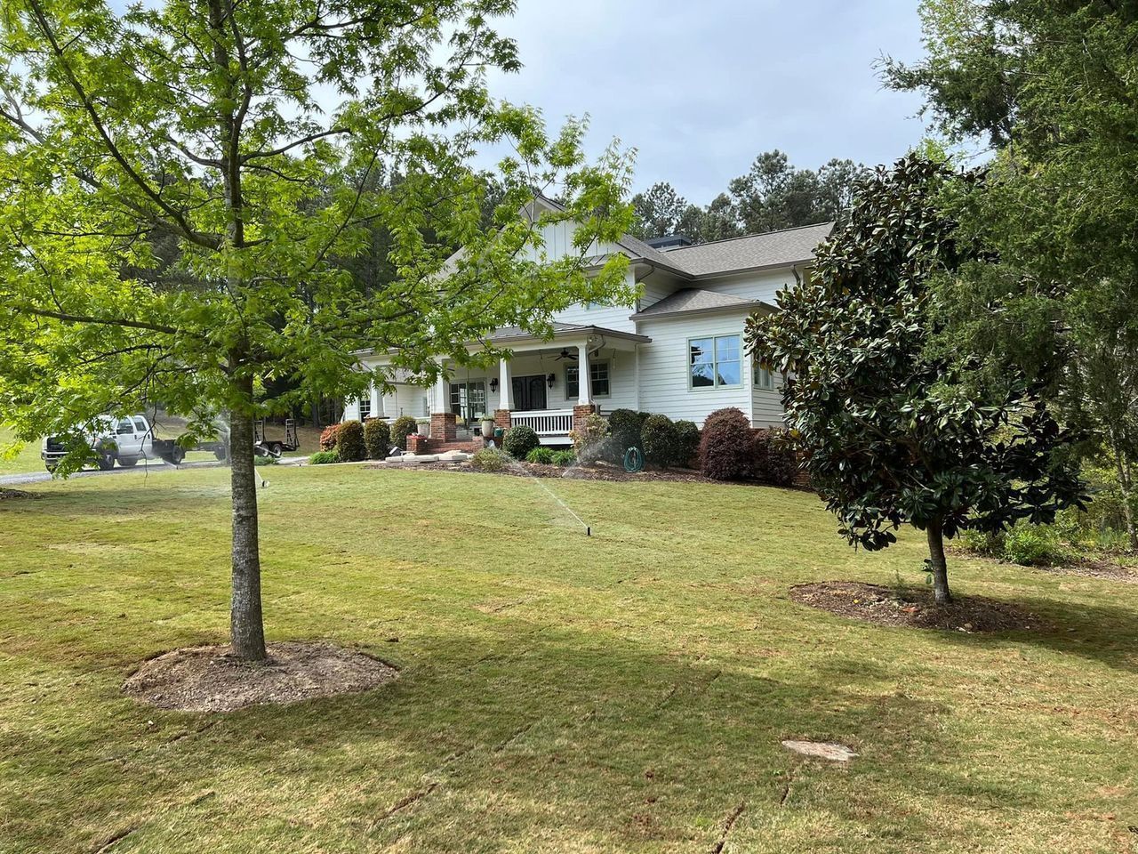 A white house with a large lawn and trees in front of it.