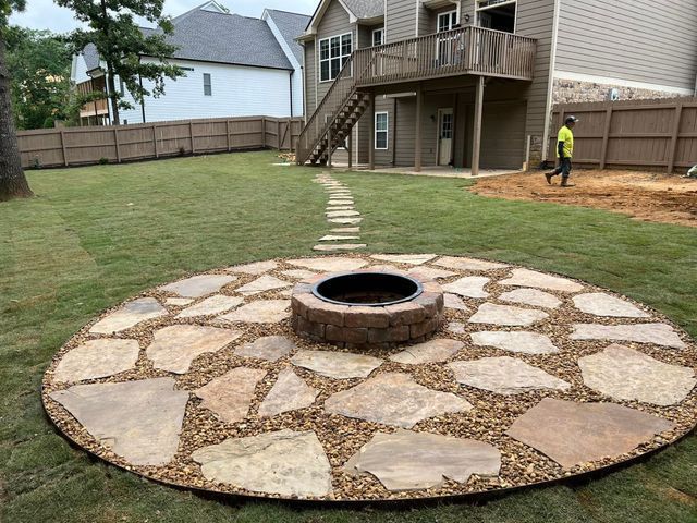 A fire pit is in the middle of a stone patio in a backyard.