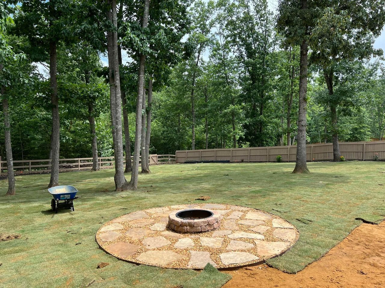 A fire pit in the middle of a lush green field surrounded by trees.