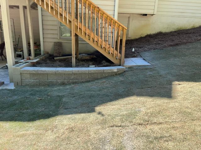 A wooden deck with stairs leading up to it is in the backyard of a house.