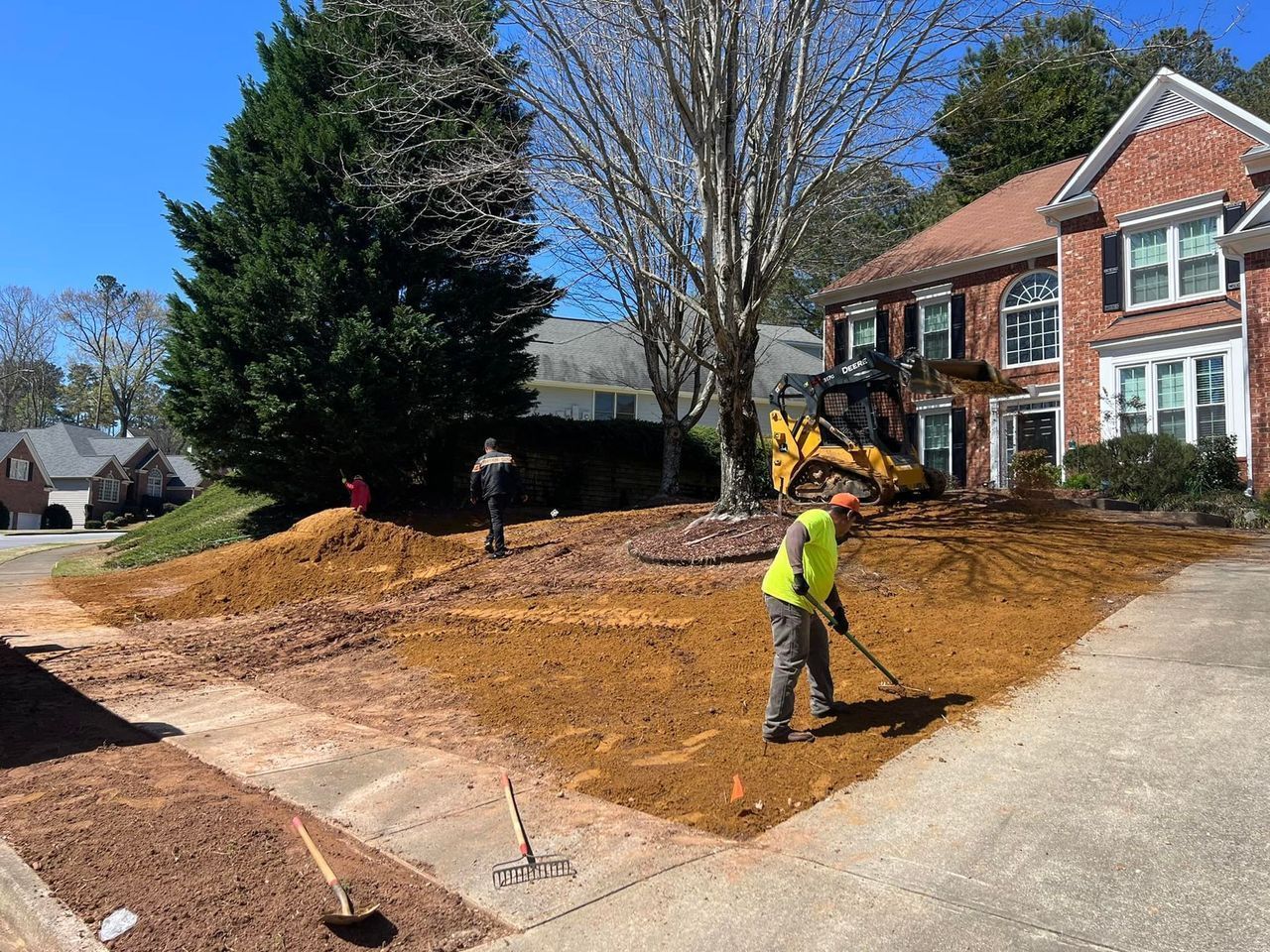 A man is raking dirt in front of a house.