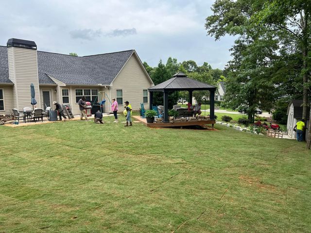 A group of people are standing in front of a gazebo in a backyard.