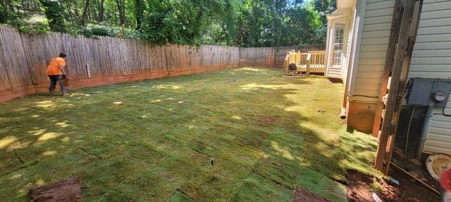 A man is raking a lush green lawn in front of a house.
