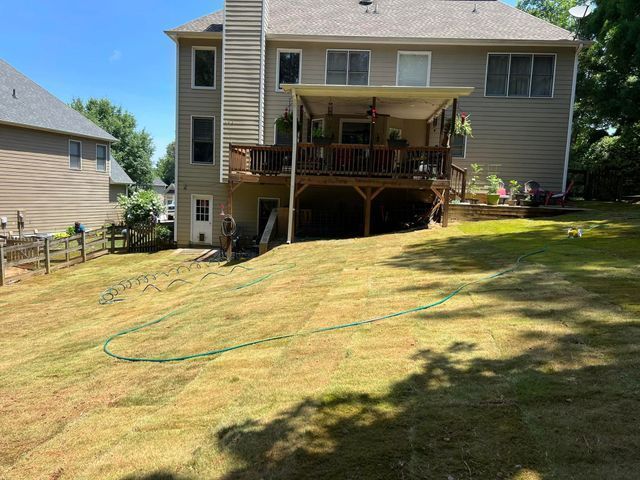 The backyard of a house with a large deck and a hose in the grass.