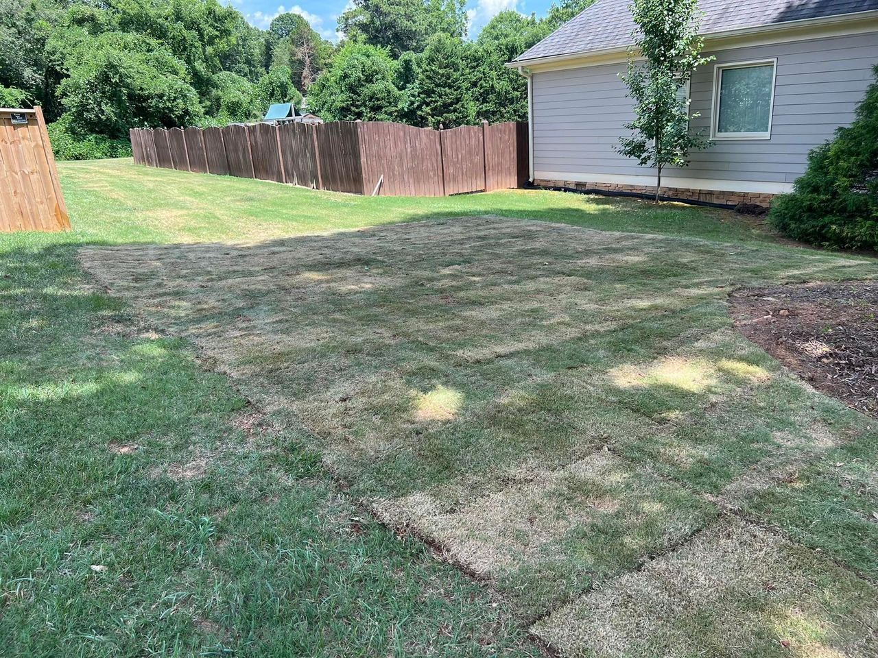 A lawn with a fence and a house in the background.