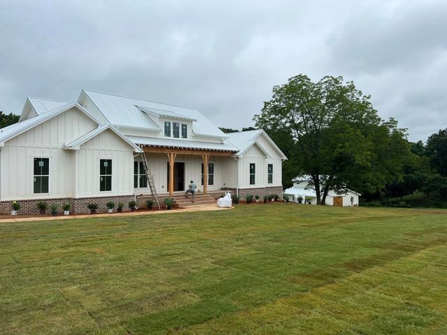 A large white house is sitting on top of a lush green field.