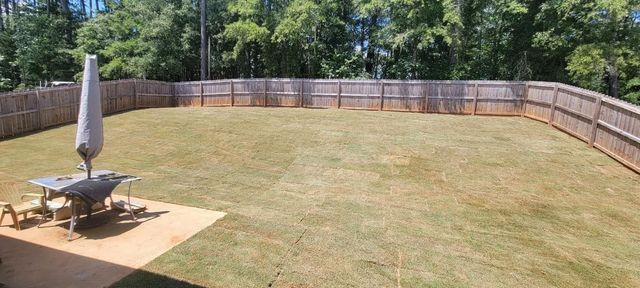 A large lawn with a wooden fence and a table and umbrella in the middle.