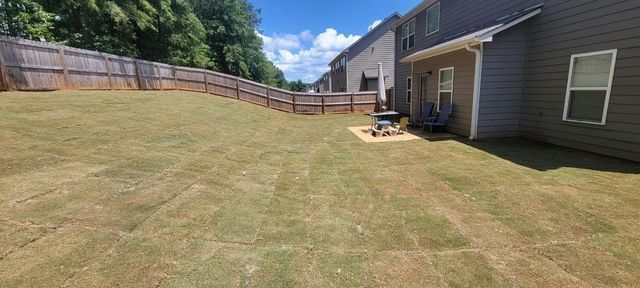The backyard of a house with a large lawn and a fence.