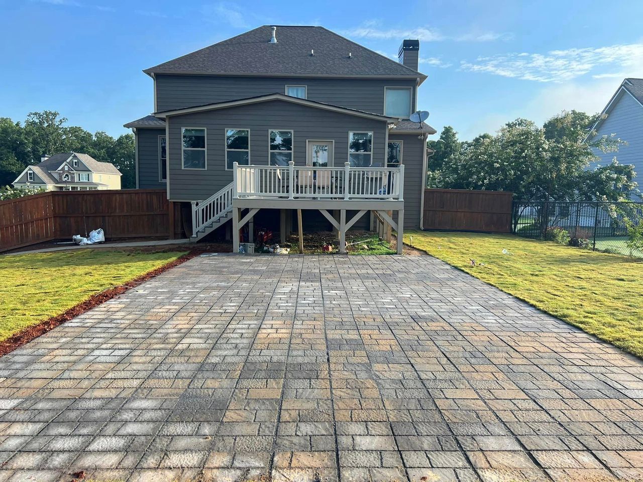 A brick driveway leading to a large house with a deck.