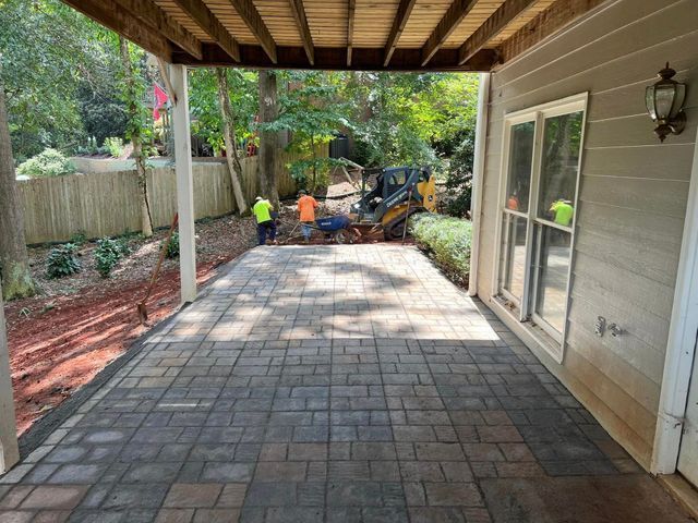 A group of men are working on a patio under a wooden deck.