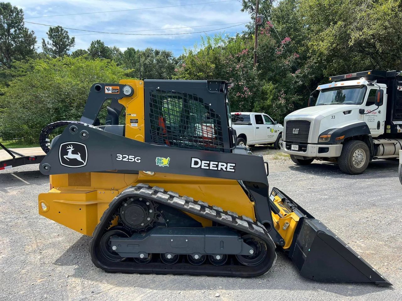 A yellow and black tractor is parked in a gravel lot next to a tow truck.