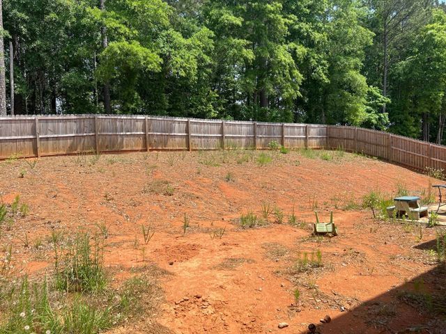 A large dirt field with a wooden fence and trees in the background.