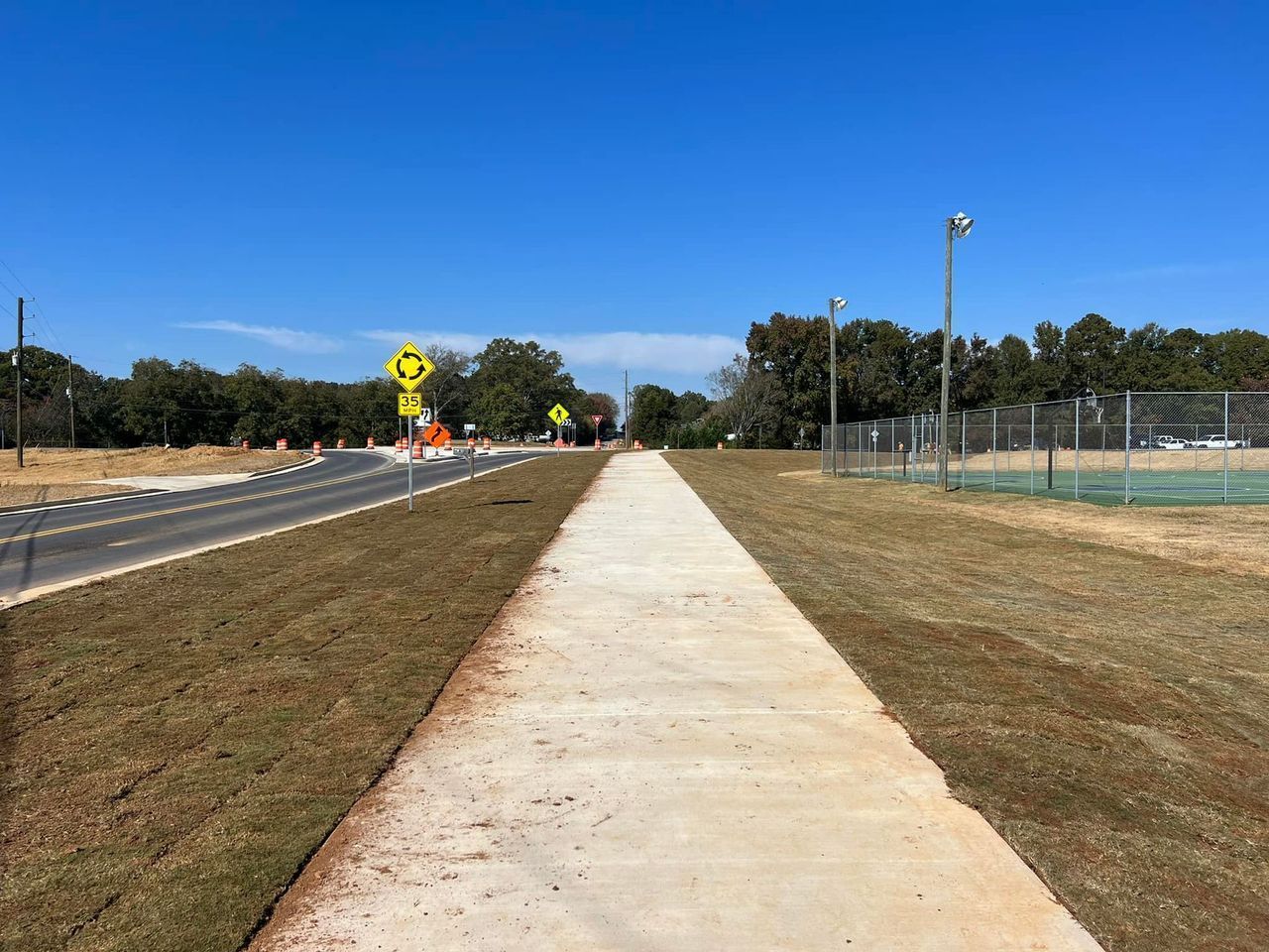 A concrete walkway going through a grassy field next to a road.