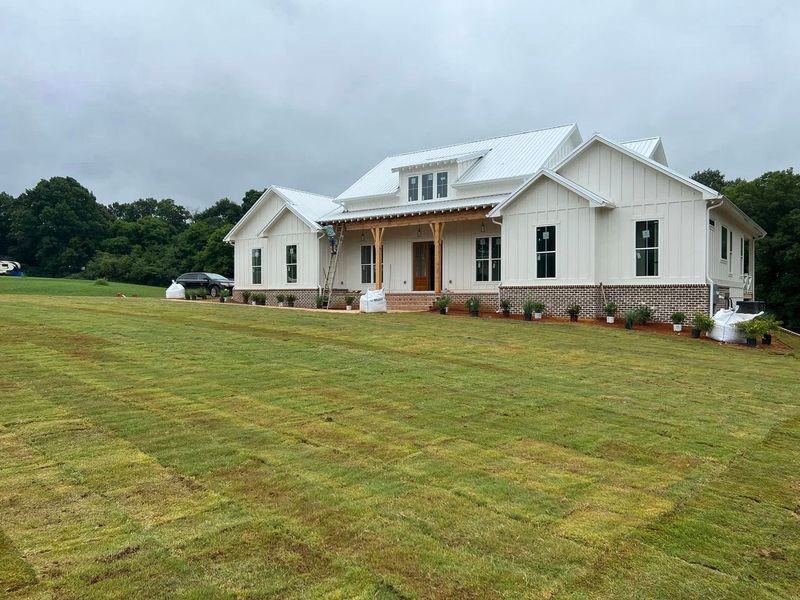 A large white house is sitting on top of a lush green field.