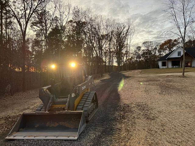 A bulldozer is driving down a dirt road in front of a house.
