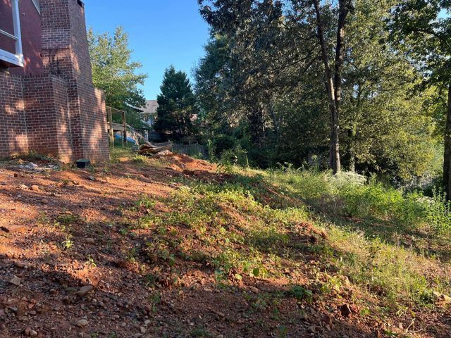 A brick house is sitting on top of a dirt hill surrounded by trees.