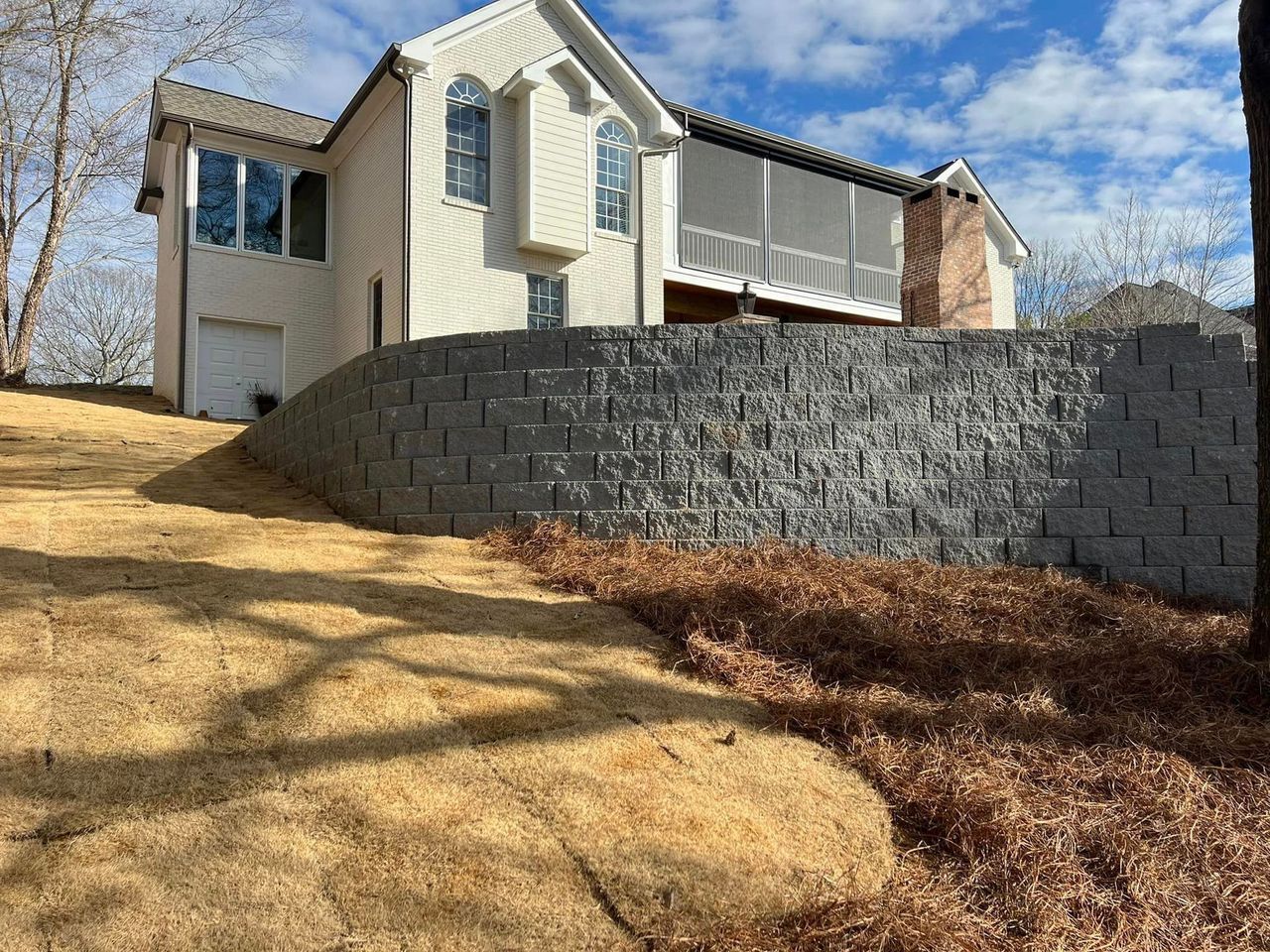 A large white house is sitting on top of a hill next to a brick wall.