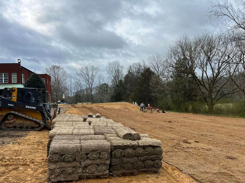 A bulldozer is driving down a dirt road next to a pile of bricks.