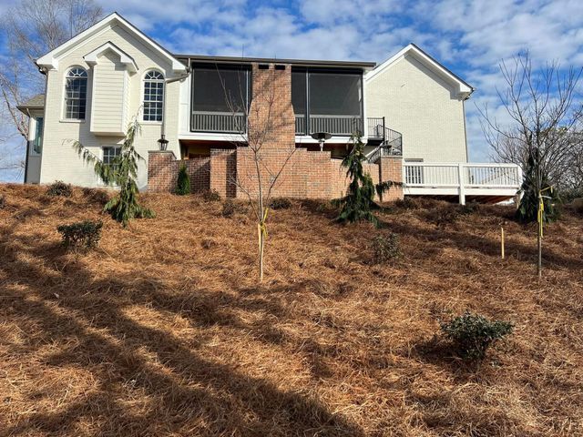 A large white house with a screened in porch sits on top of a hill.