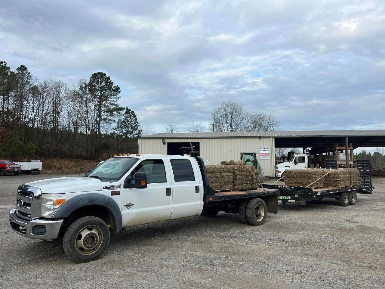 A white truck with a flatbed trailer is parked in a gravel lot.