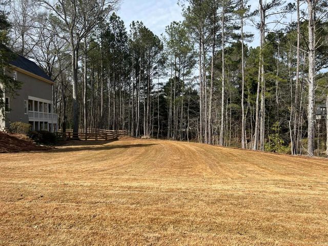 A dirt road going through a forest with a house in the background.
