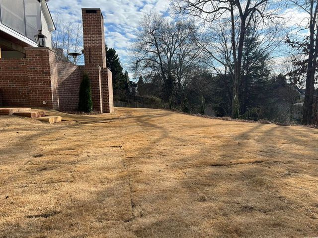 A lawn with a chimney in the background and a house in the background.