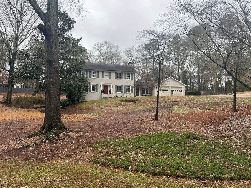 A large white house is surrounded by trees and grass on a cloudy day.