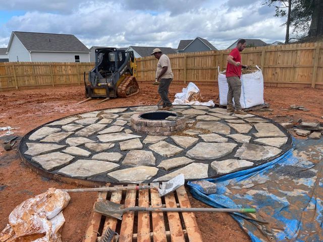 Two men are working on a fire pit in a backyard.