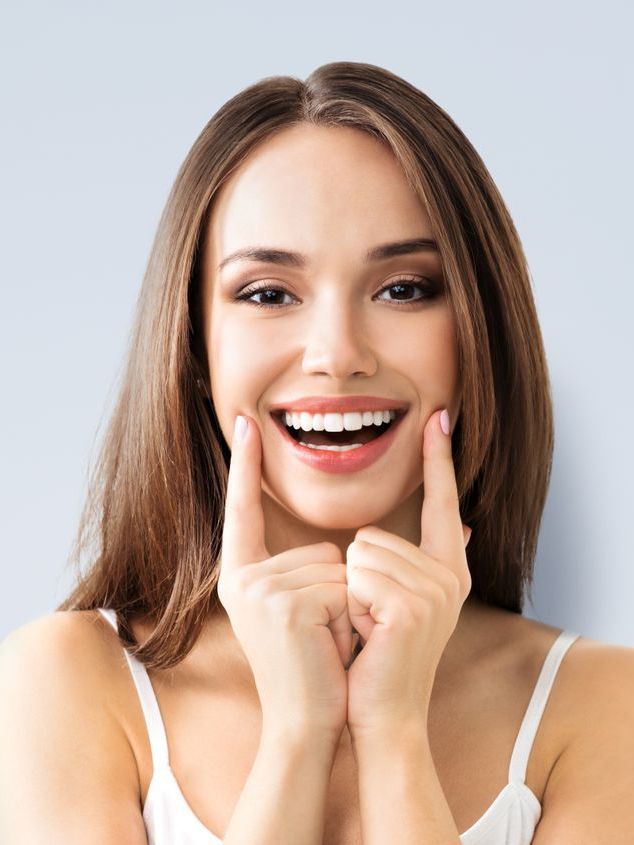 A woman is smiling and touching her face with her hands.