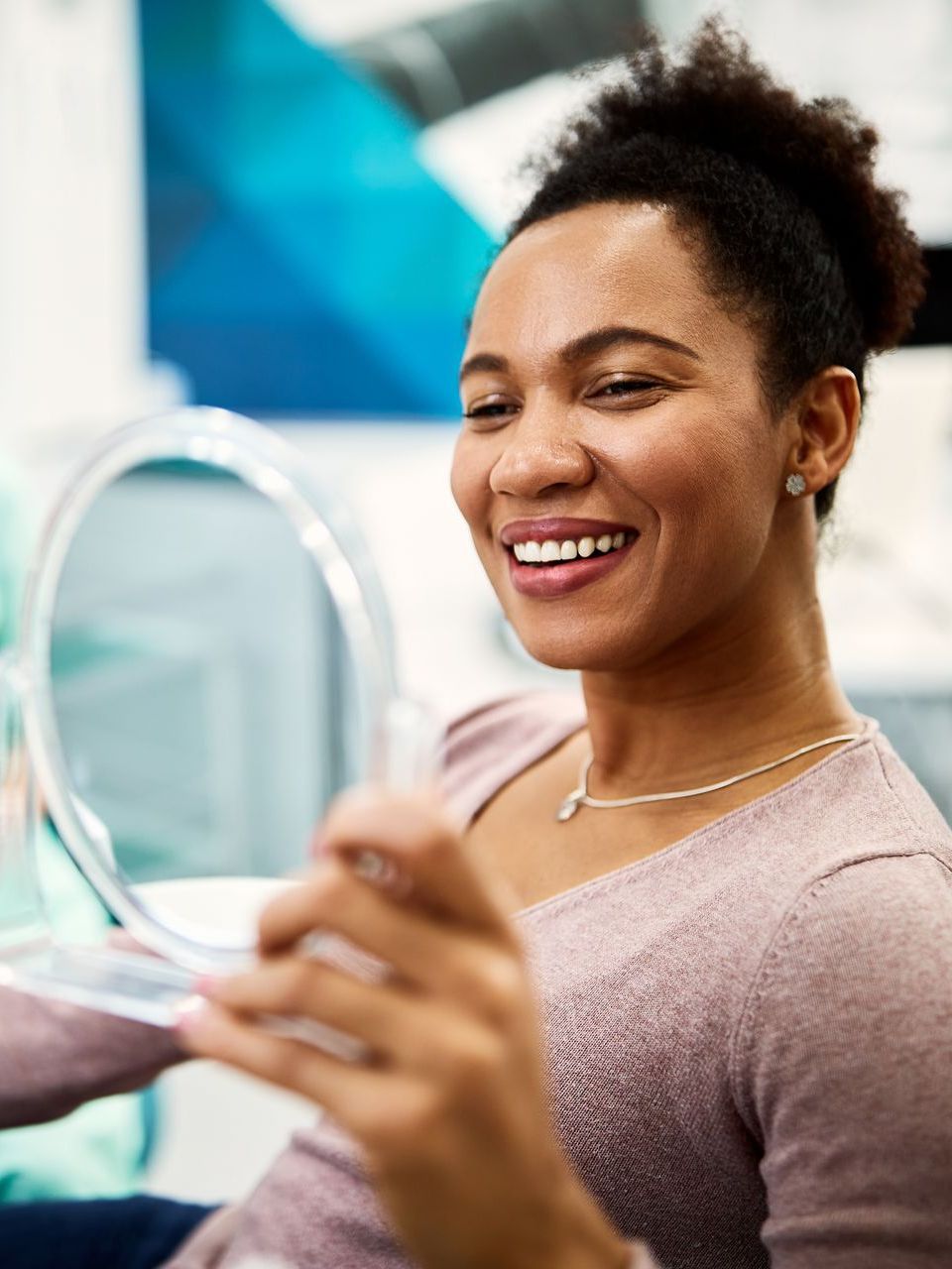 A woman is smiling while looking at her teeth in a mirror.