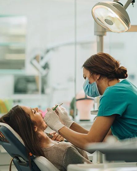 A woman is sitting in a dental chair getting her teeth examined by a dentist.