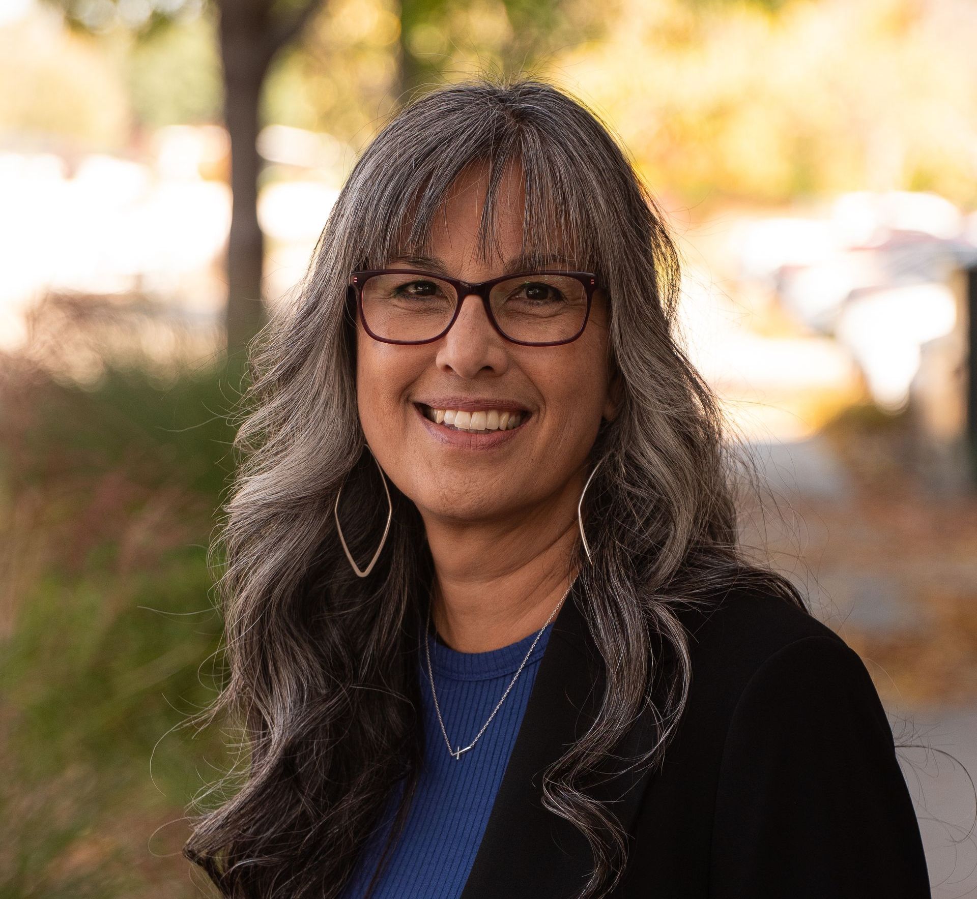 A woman wearing glasses and a blue shirt is smiling for the camera.