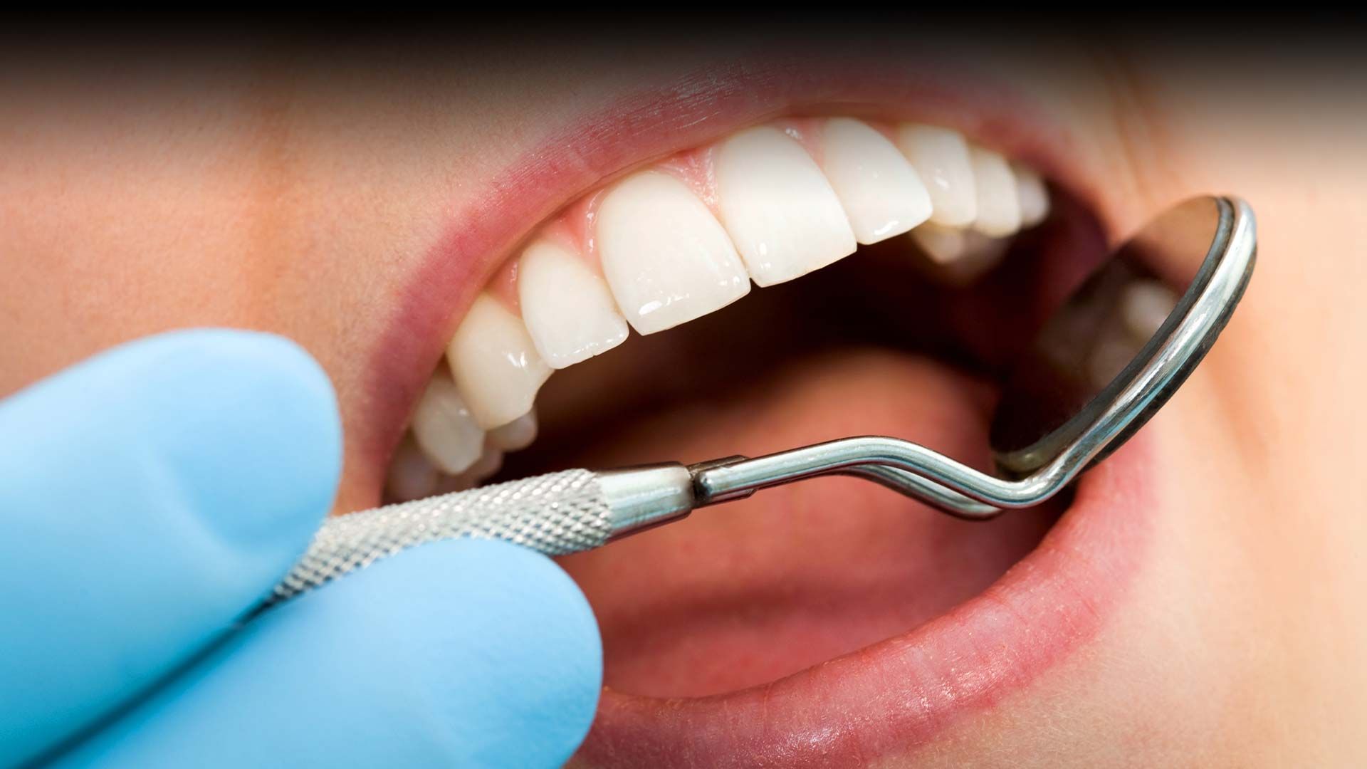 A dentist is examining a woman 's teeth with a mirror.