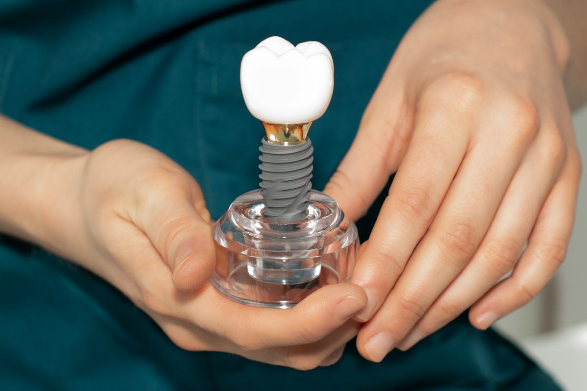 Hands holding a dental implant model with a white tooth crown on a clear base