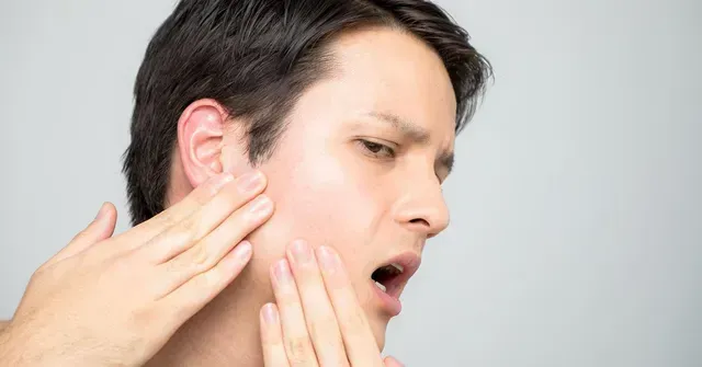 Man with pained expression touching his cheek; possible jaw pain.