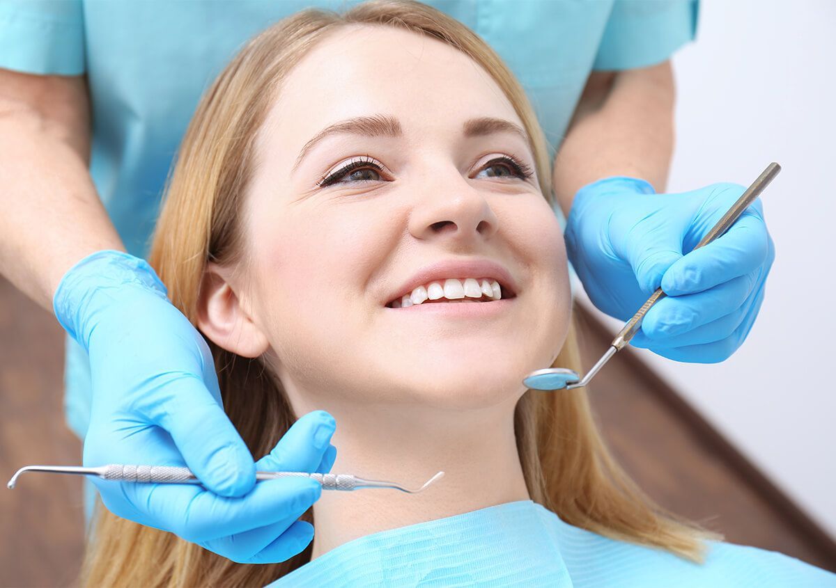 Woman smiling during dental exam; dentist using tools.