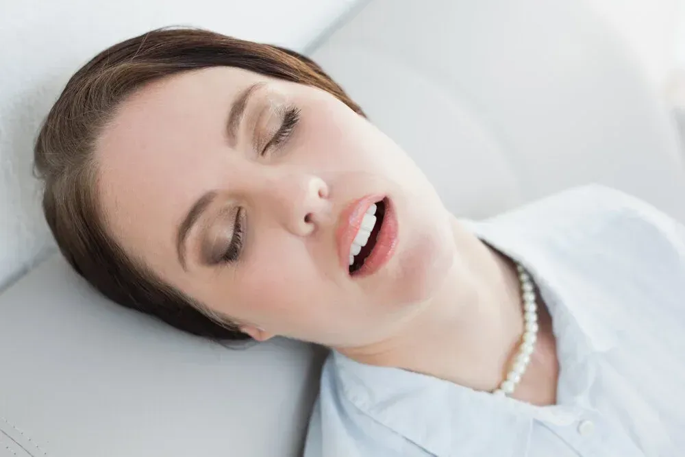 Woman asleep, head on a couch, mouth slightly open.