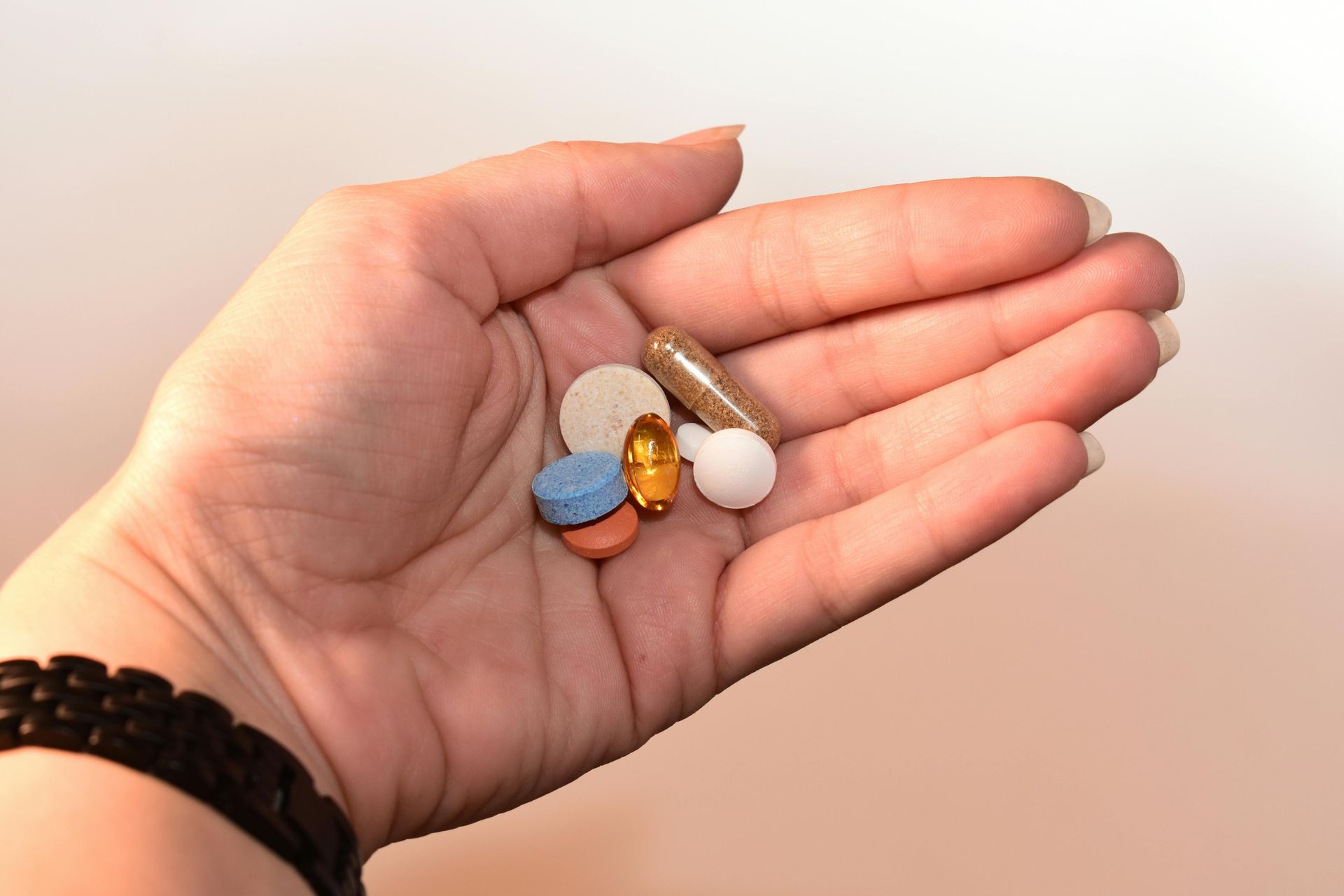 A person is holding a handful of pills in their hand.