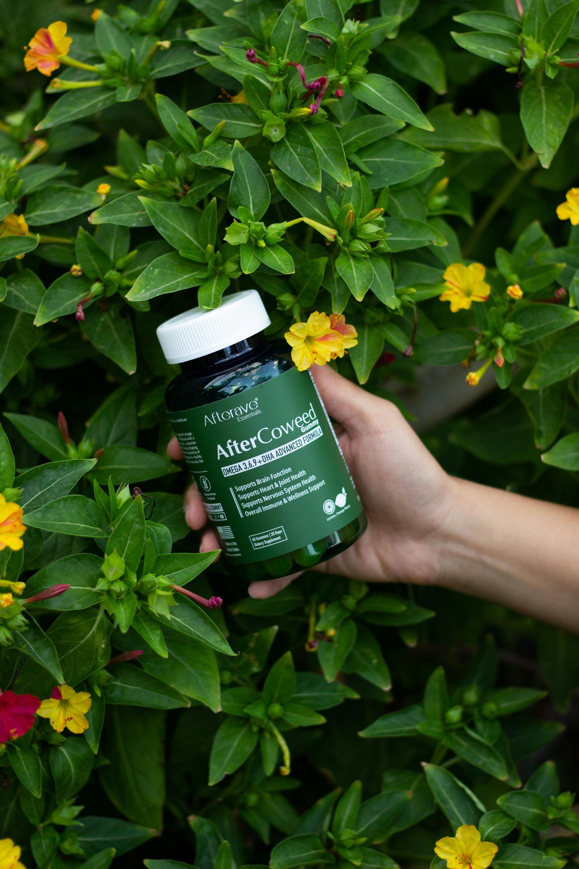 A person is holding a bottle of pills in front of a bush of flowers.