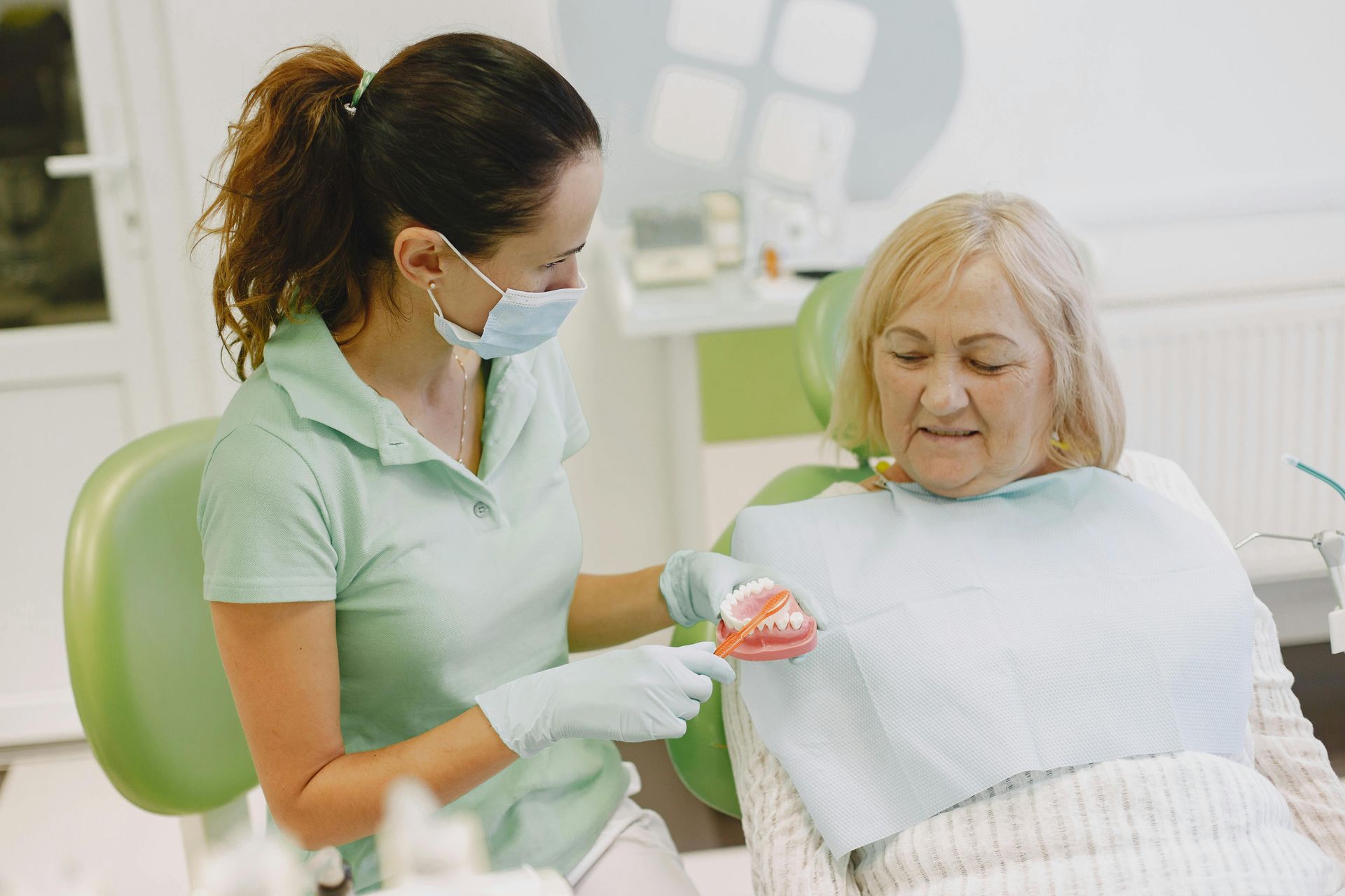 Dental assistant showing a model of teeth to patient in chair discussing treatment