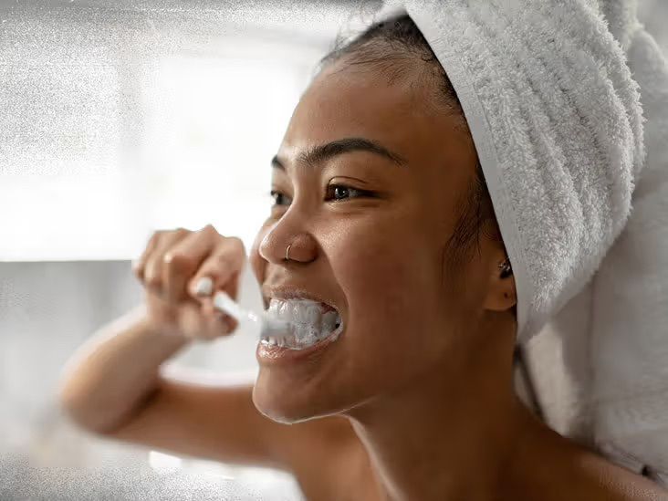 A woman with a towel wrapped around her head is brushing her teeth.