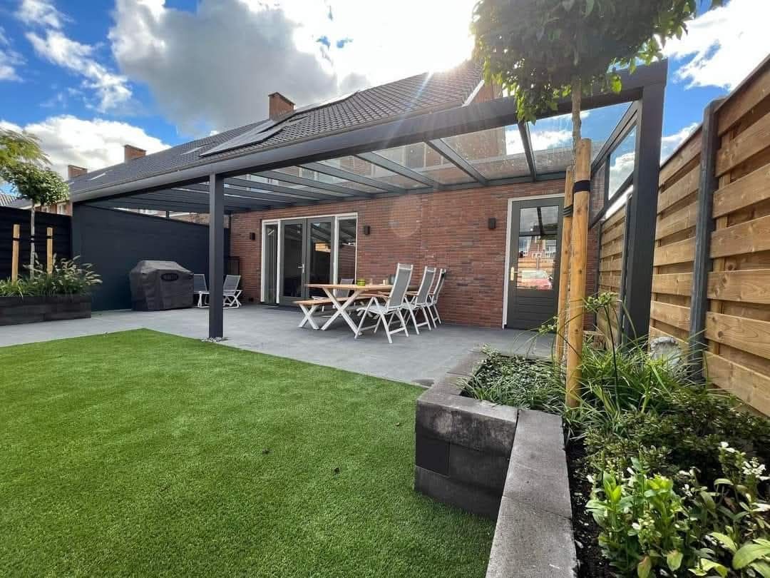 Een terras met een tafel en stoelen onder een pergola in een achtertuin. Veranda Nijmegen Arnhem Overkapping Gelderland Overijssel Limburg Glazen schuifwand