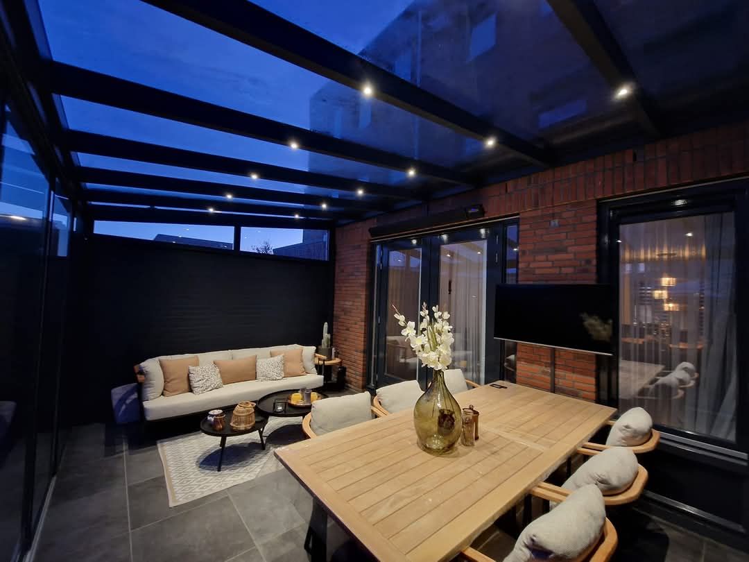 In het midden van de kamer staat een tafel met daarop een vaas met bloemen. Veranda Nijmegen Arnhem Overkapping Gelderland Overijssel Limburg Glazen schuifwand