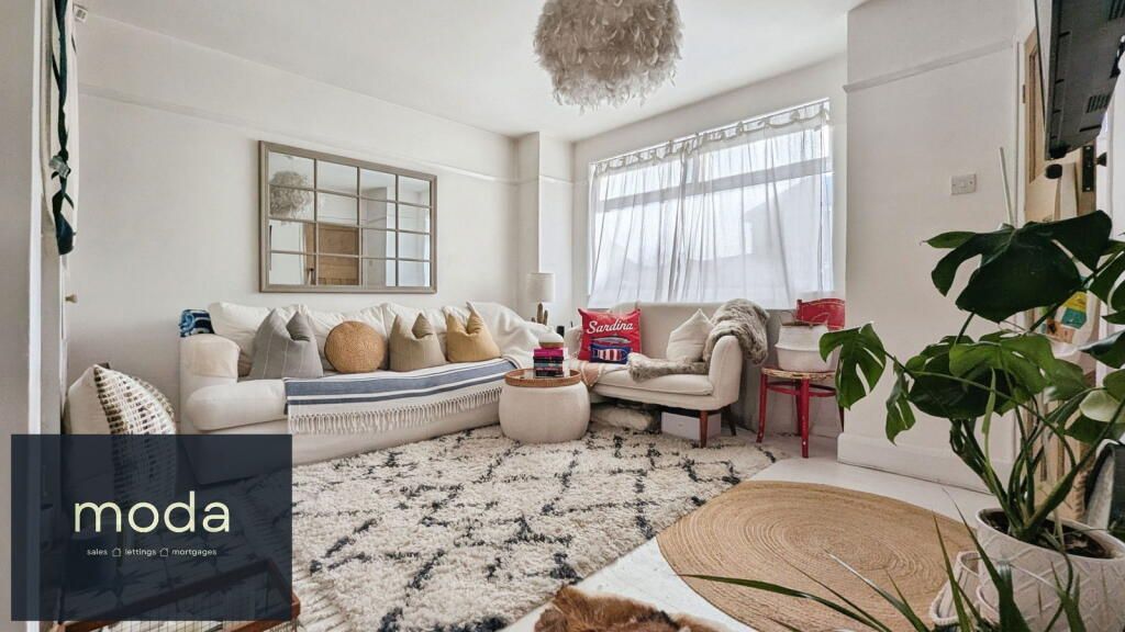 Cozy living room with a white sofa, patterned rug, and large plant. Bright and airy with natural light.