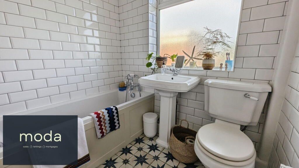 Bathroom with white subway tile, pedestal sink, and patterned floor tile; window with plants.