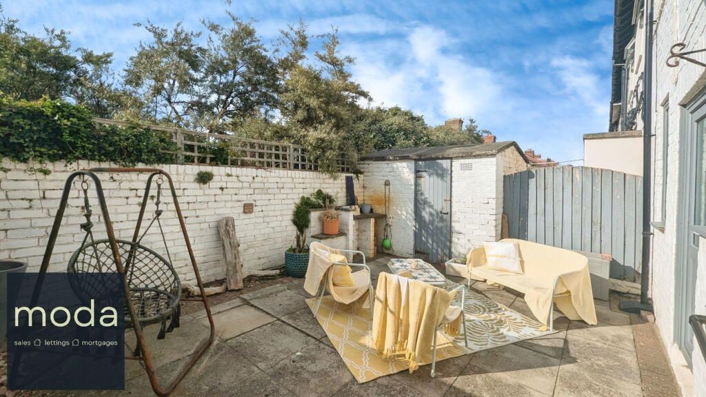 Backyard patio with swing, covered seating, and a shed, under a blue sky.