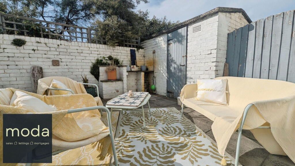 Outdoor seating area with white brick walls, a grey shed, and a patterned rug.