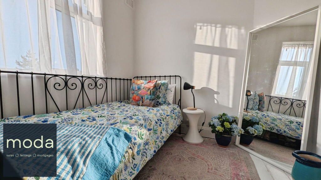 Bedroom with single bed, white walls, sheer curtains, large mirror.