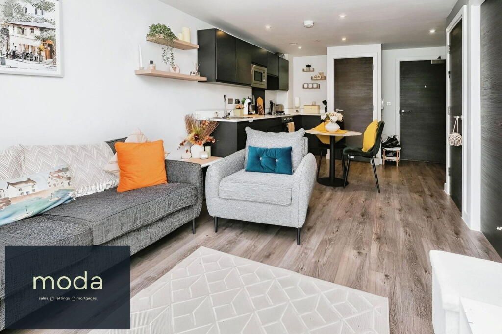 Modern apartment interior with open kitchen, dining area, living room. Gray sofa, armchair, wooden floor.